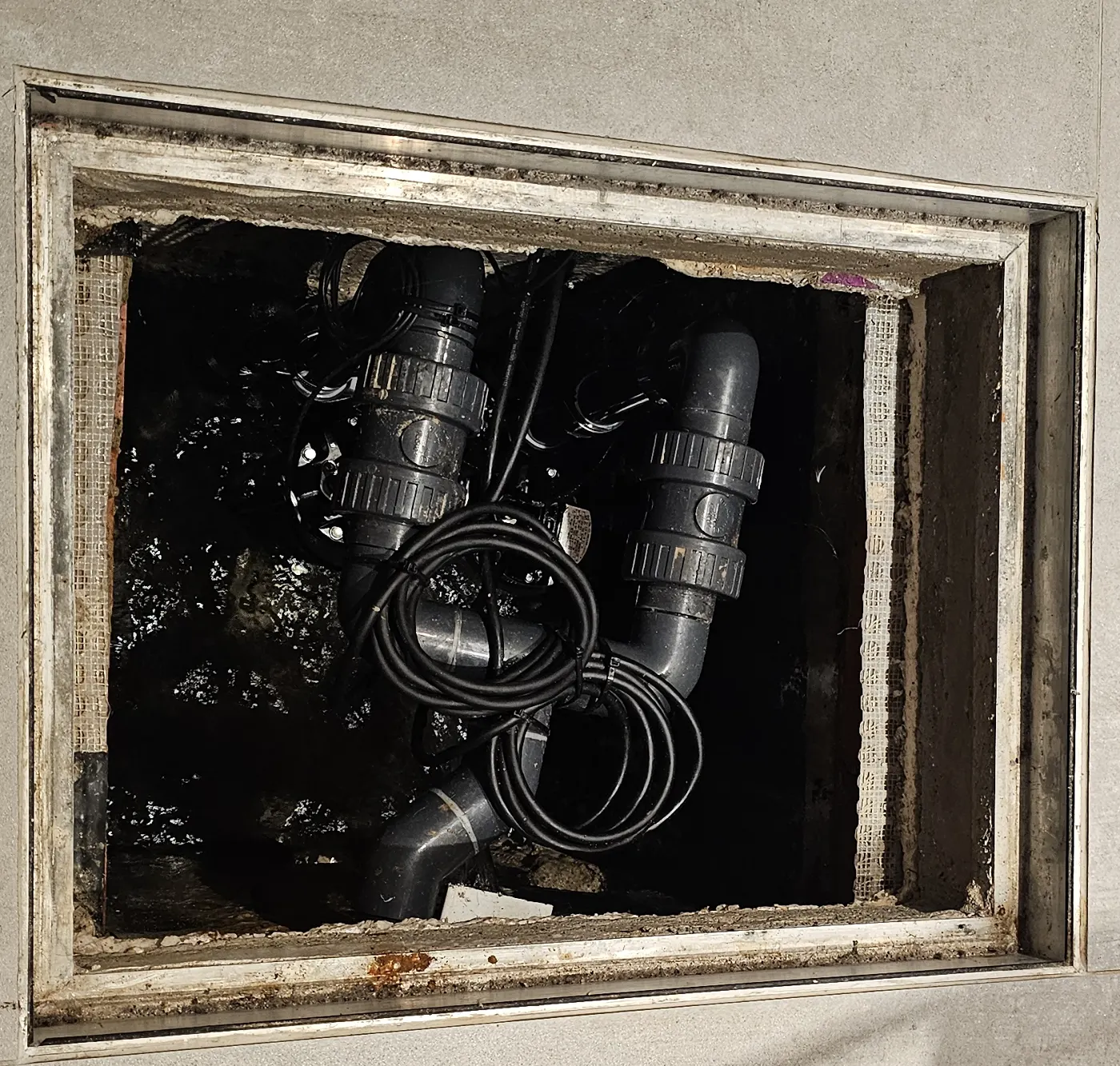 A basement pump sump with the access cover removed. Two pump risers, each fitted with its own valves, join into a single discharge pipe inside the chamber.